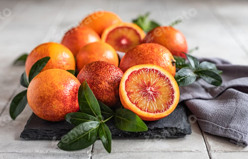 Preview: Sliced and whole ripe juicy Sicilian blood oranges with leaves on black stone board. Seasonal fruits