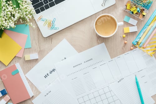 Preview: top view of planners, stationery, cup of coffee and laptop on wooden table