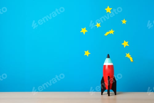 Preview: Bright toy rocket on wooden desk. Space for text