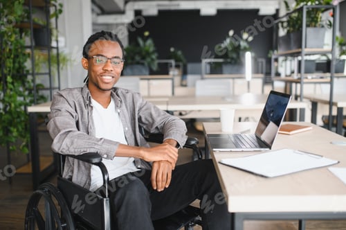 Preview: Smiling african american manager sitting in wheelchair working on laptop in modern office