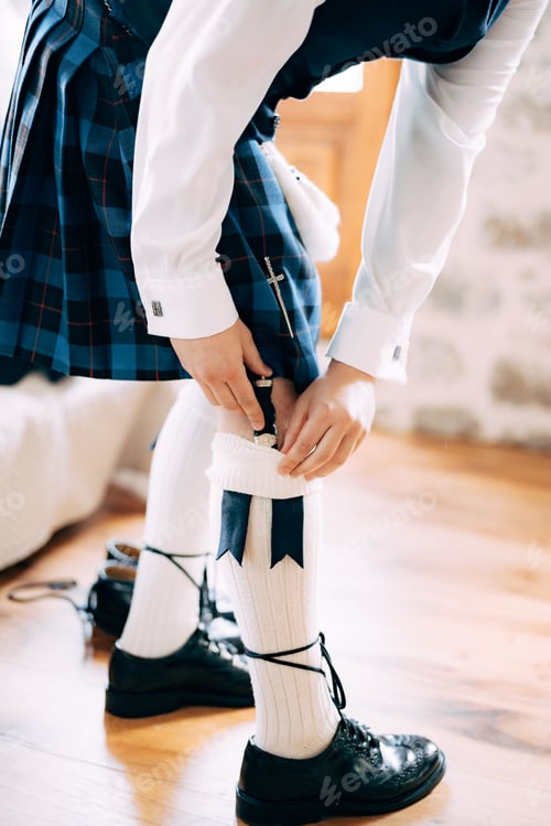 Preview: A man in Scottish national dress prepares for a wedding ceremony in a hotel room and putting sgian