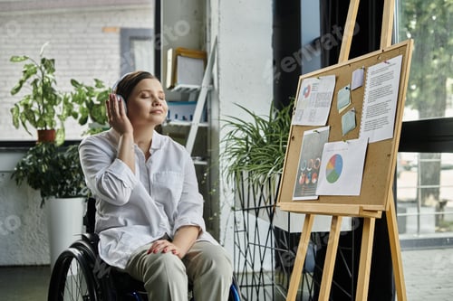 Preview: Young businesswoman in wheelchair listening to music in modern office