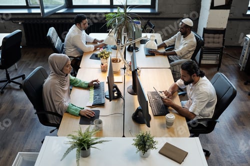 Preview: Four young co-workers sitting by tables in front of computers