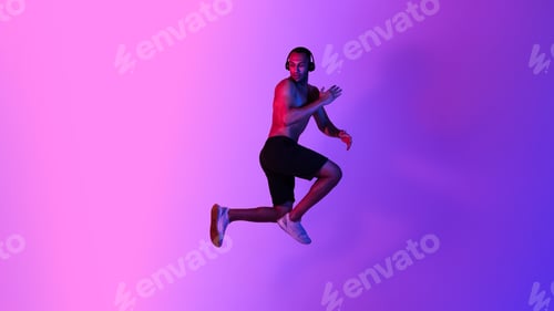 Preview: Athletic African American Male Jumping Wearing Headphones Over Purple Background