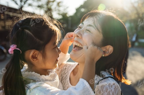 Preview: Daughter pulling cheeks of laughing mother outdoors
