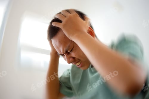 Preview: Young Asian man suffering from migraine at home