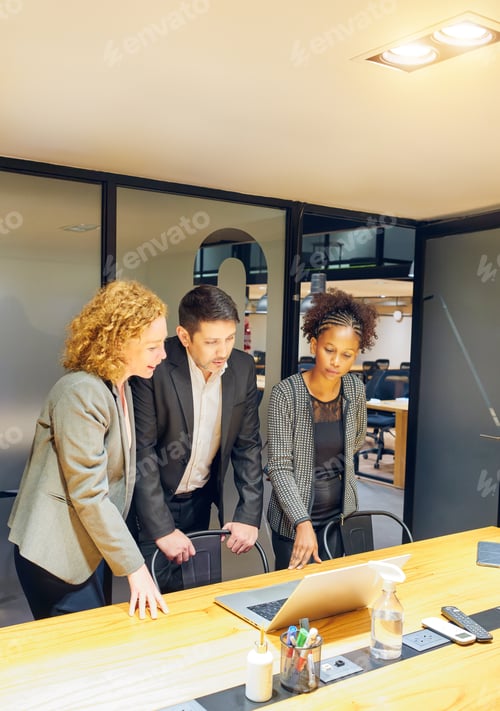 Preview: three multiracial business people standing working looking at a laptop in a meeting room