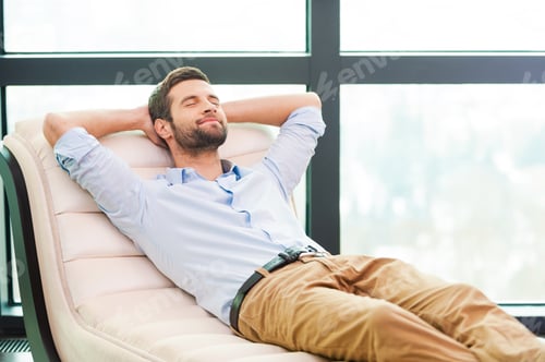 Preview: Handsome day dreamer. Handsome young man holding hands behind head while sleeping on the couch