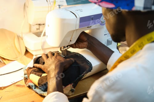 Preview: African tailor sewing a hat with sewing machine at sewing workshop.
