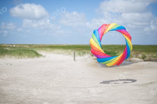 Preview: Beautiful shot of a person holding a colorful round kite in the sandy shore under the calm sky
