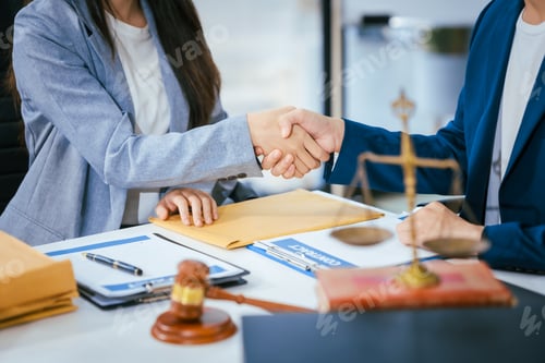 Preview: A male lawyer is shaking hands with a female client at a desk in a law office They finalize a deal