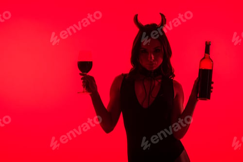 Preview: sensual girl in Devil costume holding glass and bottle of wine, isolated on red