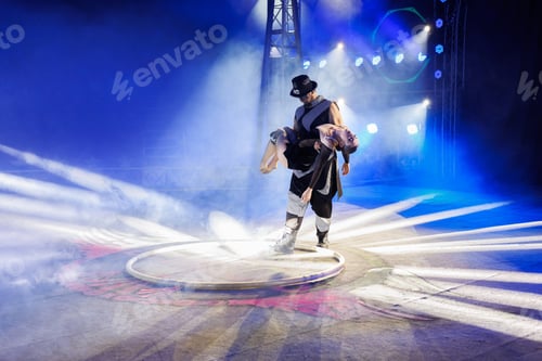 Preview: Aerialist performs on a gymnastic hoop under dome of the circus under the light of blue spotlights.