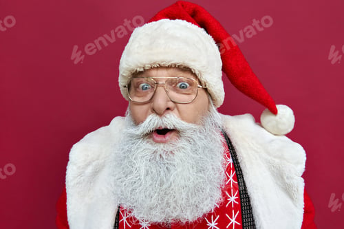 Preview: Surprised excited funny Santa Claus wearing costume isolated on red background.