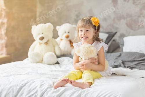 Preview: Portrait of child girl having fun sitting and playing with a teddy bears on a bed.