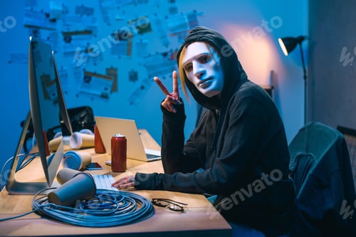Vista previa: female hacker in mask showing v sign at workplace