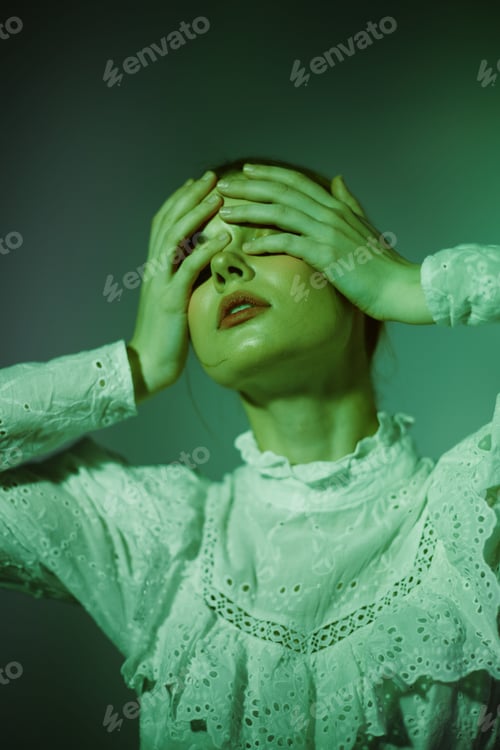 Preview: A young female model in a white lace blouse, expressing anguish with her hands on her head against a