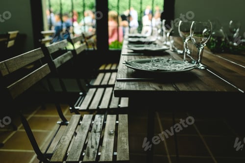 Preview: Wooden tables with cutlery plates and backlit glasses without anyone.