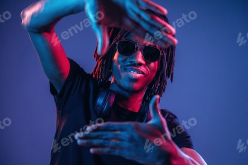 Preview: Gesture of capturing the photo. African American guy is studio with neon lighting