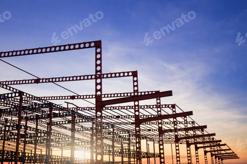 Preview: Silhouette of metal structure of large industrial building in construction site against sunset sky