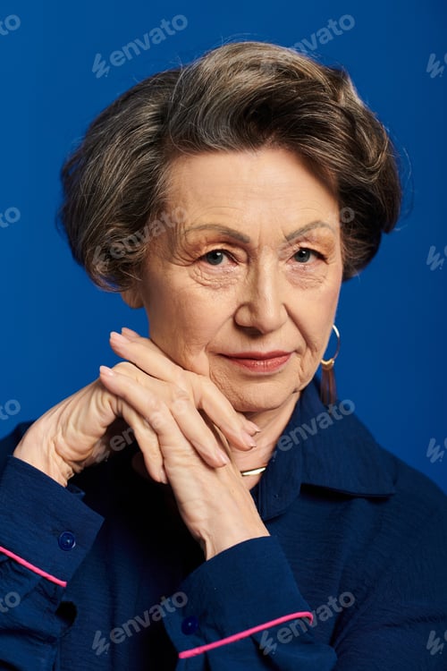 Preview: A stylish woman in her 60s poses gracefully against a striking blue background.
