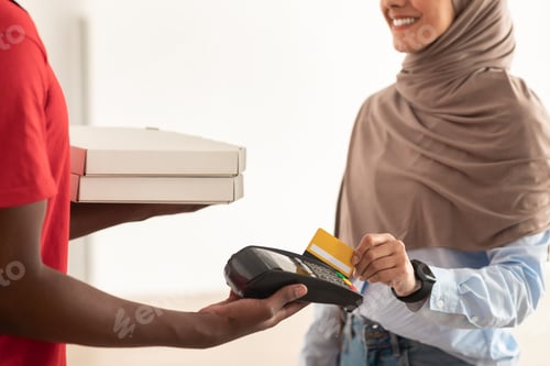 Preview: Deliveryman holding POS machine, muslim woman paying with card