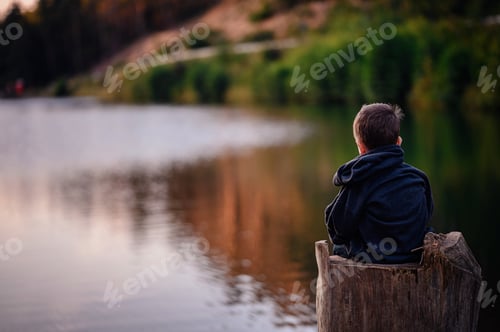 Preview: Boy Sitting on Tree Stump Gazing at Calm Lake