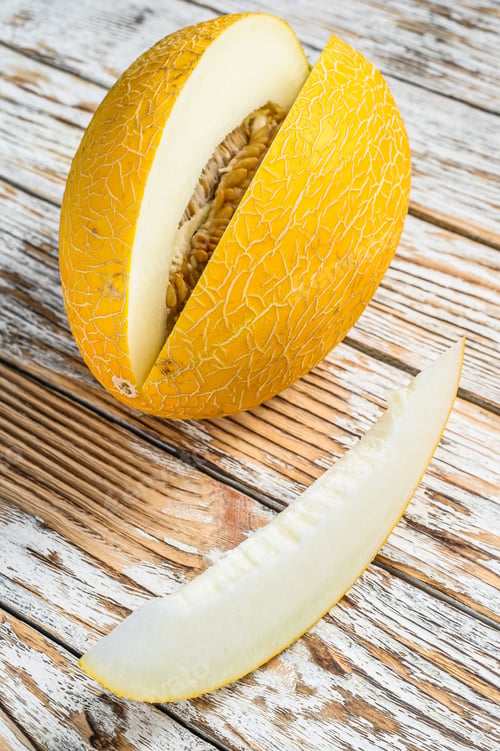 Preview: Yellow ripe cut melon. White wooden background. Top view.