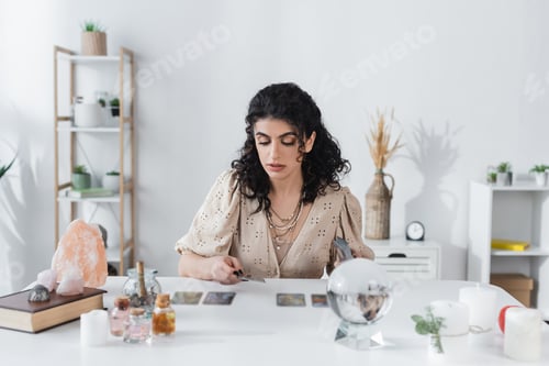 Vista previa: adivina gitana con cartas del tarot cerca de velas y suministros de brujería sobre la mesa