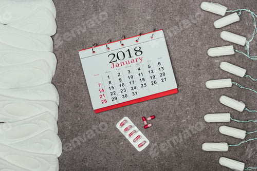 Preview: top view of arranged menstrual pads and tampons, calendar and pills on grey surface