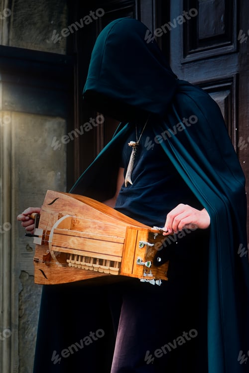 Preview: Closeup of a man in a cloak holding a hurdy gurdy medieval instrument