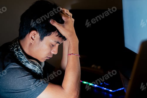Preview: Stressed young man in front of computer in dimly lit room