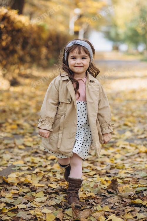 Preview: Happy and beautiful little girl in a beige coat walks in the autumn park