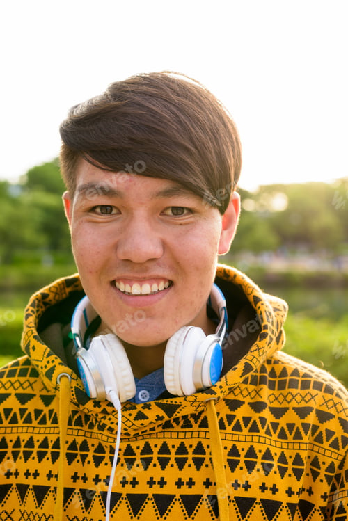 Preview: Young Asian teenage boy wearing headphones while relaxing at the