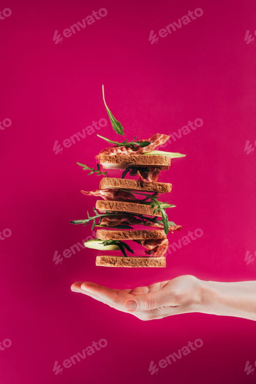 Preview: partial view of female hand and levitating sandwiches isolated on pink