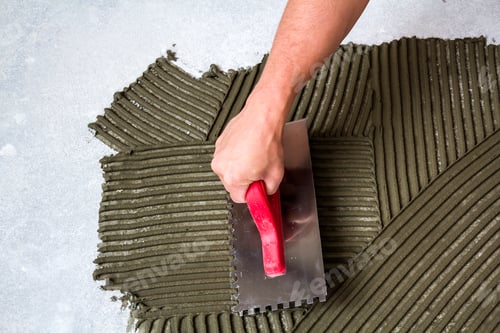 Preview: Worker hand with trowel tool for tiles installation making mortar adhesive on floor