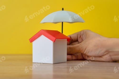 Preview: A toy house is being sheltered by a miniature umbrella held by a hand.