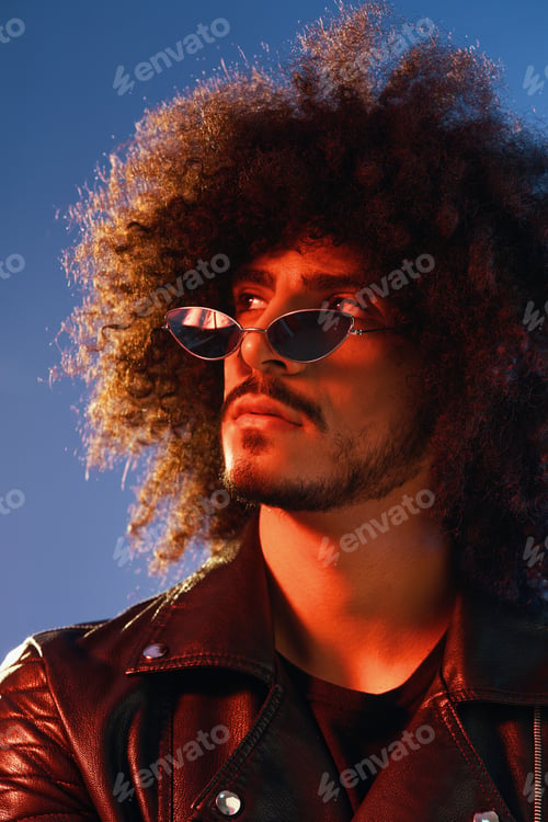 Preview: Portrait of a stylish man with curly hair on a blue background multinational, colored light, trendy