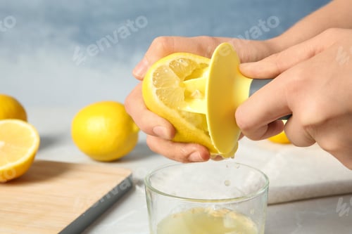Preview: Woman squeezing lemon juice with reamer into glass on table