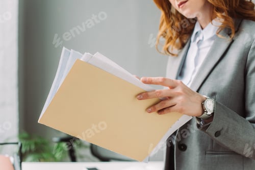 Preview: Cropped view of businesswoman leafing through paper sheets in folder with blurred workplace on