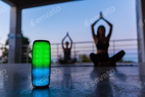 Preview: wireless speaker on foreground of company of friends doing yoga listening to music in dusk