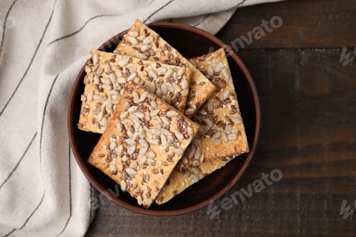 Preview: Cereal crackers with flax, sunflower and sesame seeds in bowl on wooden table, top view