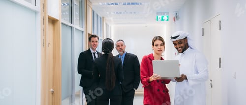 Preview: A group of different business people are sitting around a big meeting table in a modern office.
