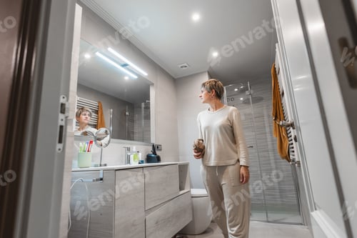 Preview: Woman looking in bathroom mirror during morning routine