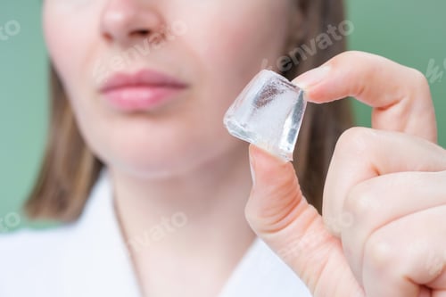 Preview: Young woman holding ice cube near her face on green background.