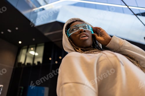 Vorschau: Futuristische junge Frau mit Neonbrille und Hoodie in urbaner Umgebung