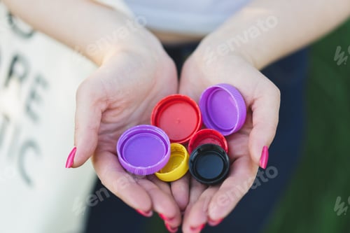 Preview: Woman hands are holding a handful of multi-colored plastic lids. Concept of environmental pollution