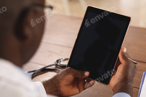 Preview: Mid section of african american senior male doctor holding digital tablet with copy space at home