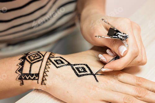 Preview: young woman mehendi artist painting henna on the hand