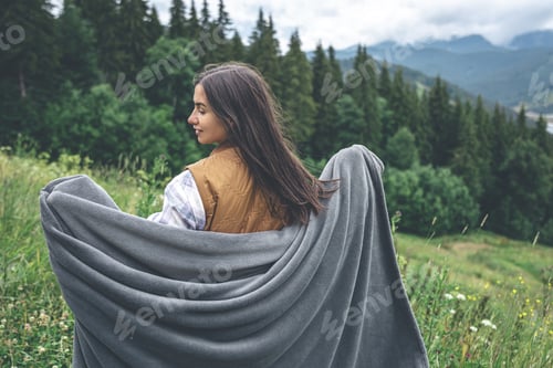 Preview: A young woman wrapped in a blanket in the mountains.